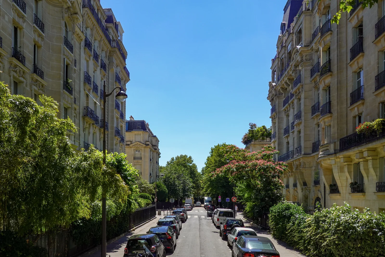 Voitures stationnées le long d'une rue parisienne bordée d'immeubles haussmanniens